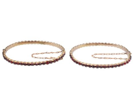 A pair of Victorian Bohemian garnet set bangles each with claw set garnets, the hinged bangles with push clasps and safety ch