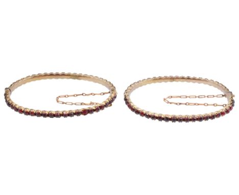 A pair of Victorian Bohemian garnet set bangles each with claw set garnets, the hinged bangles with push clasps and safety ch