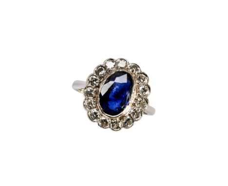 A DIAMOND AND SAPPHIRE OVAL CLUSTER RING consisting of a central oval Sapphire in rub over setting with pierced under-gallery