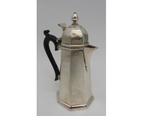 A SILVER HOT WATER JUG, tapered octagonal form with ebonised scroll handle and lid surmounted by finial, bears the mark of Ja