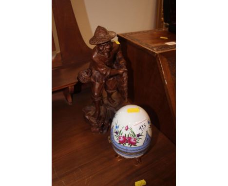 A decorative china egg shaped trinket box and a carved wooden figure holding a fishing net