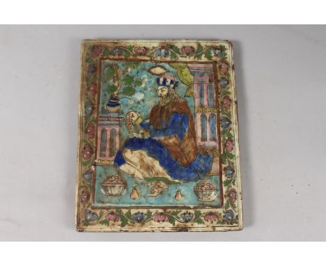 A 19TH CENTURY PERSIAN QAJAR MOULDED GLAZED POTTERY TILE, depicting a seated royal figure with foliate border, 33.5cm x 27cm.