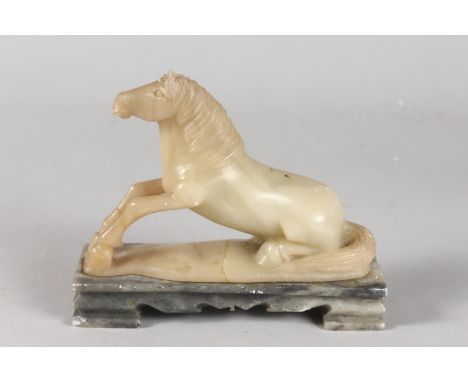 A CHINESE QING DYNASTY JADE OR GREEN SOAPSTONE CARVING OF A RECUMBENT HORSE, mounted to a rectangular hardstone base, 16cm lo