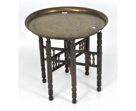 A Middle Eastern brass topped coffee table, with engraved details to the top, on folding bobbin turned wooden base, 57cm diam