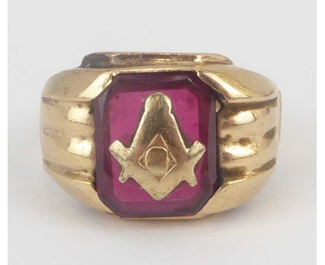 An early 20th century 10ct gold Masonic ring, with central inset gold Masonic symbol to a large square red gemstone (probably