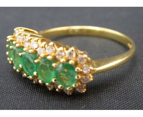 An 18ct gold emerald and diamond cluster ring, the central band of five claw set oval emeralds within a border of twenty-six 