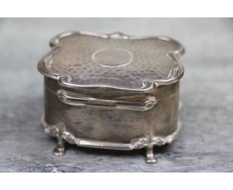 Edwardian silver trinket box of shaped form raised on four feet with stylised leaf shoulders, the hinged lid with hammered fi