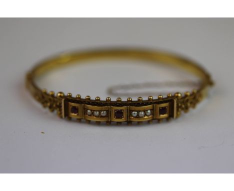 Late Victorian/ Edwardian ruby and seed pearl 15ct yellow gold hinged bangle, three small round mixed cut rubies, carré setti