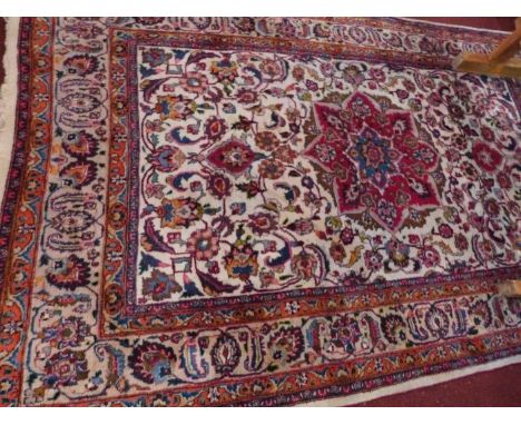 A Persian Mashad carpet with central floral medallion surrounded by floral motifs on a beige ground contained by floral borde