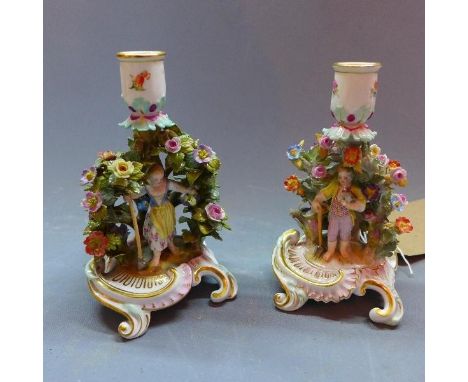 A pair of Meissen candlesticks with central figures surrounded with foliage. H.18cm 