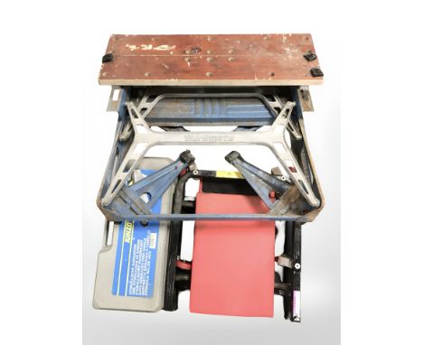 A Workmate folding bench, a boxed hydraulic roller jack and a padded inspection board on castors. 