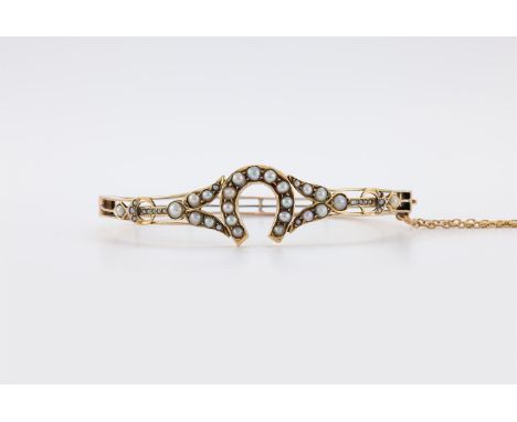 
	
		AN EDWARDIAN HORSE SHOE HALF PEARL HINGED BANGLE 
		The gold bangle with a central half pearl set horse shoe, to half pe