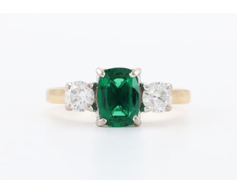 
	
		A SYNTHETIC EMERALD AND DIAMOND THREE STONE RING 
		The oval mixed cut synthetic emerald flanked by two brilliant cut di