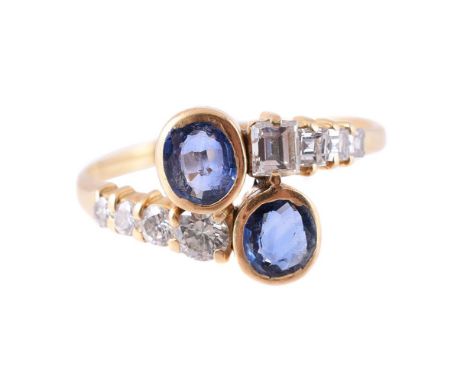 
	
		A SAPPHIRE AND DIAMOND CROSSOVER RING 
		The gold coloured band with oval cut sapphire terminals, to step cut and brilli