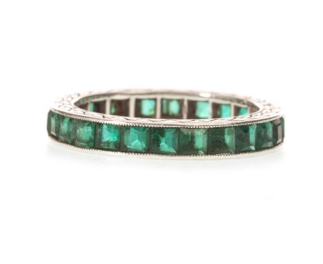 AN EARLY TWENTIETH CENTURY GREEN GEM SET ETERNITY RING, with channel set square step cut green gems, millegrain edge, with la