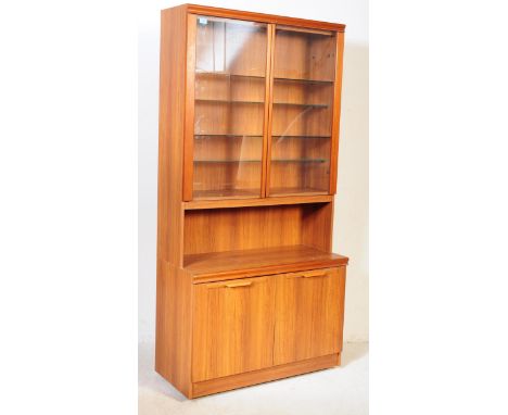 A vintage mid 20th century teak wood display bookcase cabinet. Of rectangular form with twin glazed, hinged glass doors to up