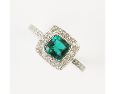 A synthetic emerald and diamond ring, comprising a central cushion cut synthetic emerald measuring 6mm x 6mm, with a surround