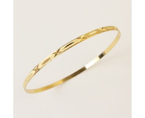 An 18ct yellow gold bangle, the round bangle with engine turned decoration to exterior, lozenge shaped '750' mark stamped to 