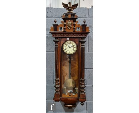 A late 19th Century walnut regulator wall clock with weight driven movement enclosed by a glazed door below an eagle pediment