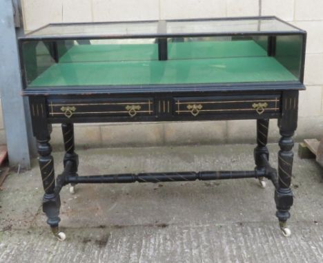 An ebonised glass display cabinet on stand, with the glazed cabinet with two drop down drawers, the base two further fitted d