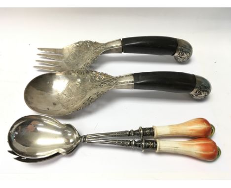 A pair of white metal and horn ornately decorated salad servers together with an additional pair of ceramic mounted silver pl