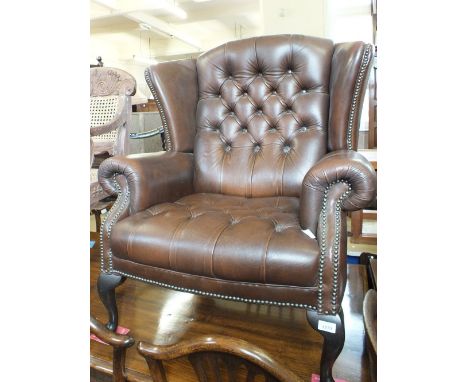 A modern brown leather button backed wing armchair with stud work