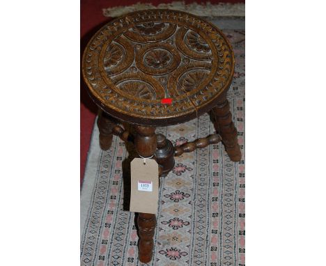 An early 20th century relief carved oak circular milking stool raised on bobbin turned supports