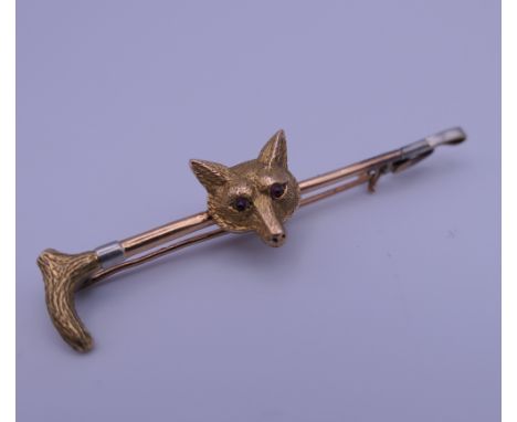 A 9 ct gold ruby set fox mask and riding crop bar brooch, housed in an Asprey box. 5.5 cm wide. 4.8 grammes total weight.