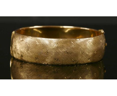 A Continental gold hinged bangle, c.1960, of 'D' section with interior rolled edges. Diamond cut star decoration to a Florent