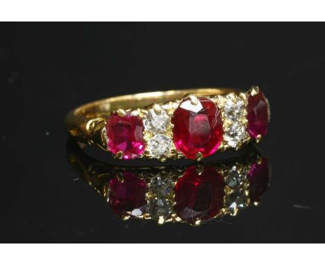 An 18ct gold synthetic ruby and diamond carved head ring, with three graduated oval mixed cut synthetic rubies, claw set in p