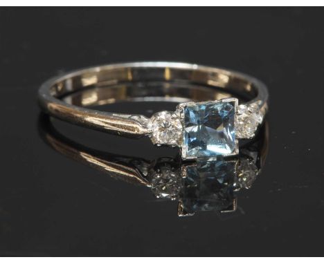 A white gold three stone aquamarine and diamond ring, with a square step cut aquamarine, claw set to a square collet. A brill