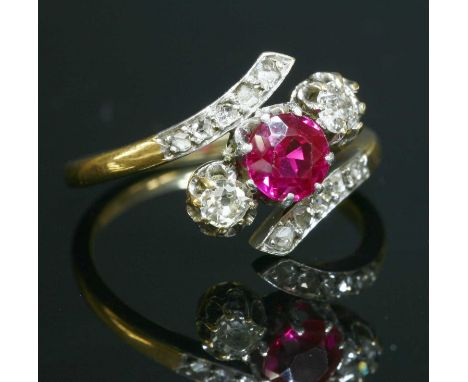 A three stone synthetic ruby and diamond crossover ring, with a circular mixed cut synthetic ruby, claw set to the centre. An