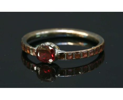 A Georgian gold flat cut garnet ring, with an oval mixed cut garnet, claw set to a plain scalloped collet. A court section ba