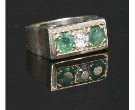 A Continental diamond and emerald three stone ring, c.1940, with an old European cut diamond, grain set between two circular 