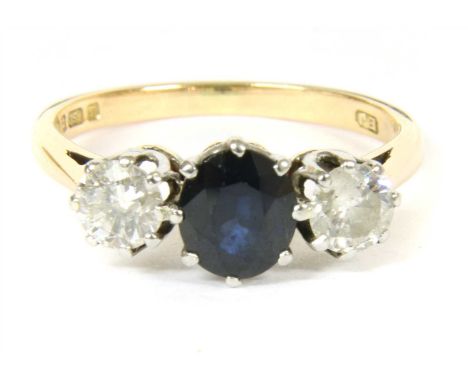 An 18ct gold three stone sapphire and diamond ring, with an oval mixed cut sapphire, claw set to a white collet at the centre