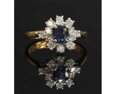 An 18ct gold sapphire and diamond oval cluster ring, with a diamond at each shoulder. An oval mixed cut sapphire, four claw s