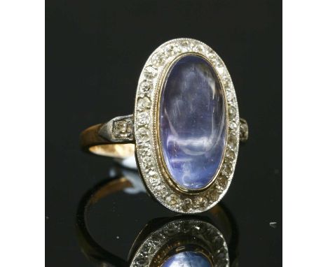A sapphire and diamond oval cluster ring, with an oval cabochon sapphire, rub set to the centre, in a yellow collet. A border