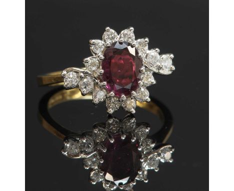 An 18ct gold ruby and diamond crossover cluster ring, with an oval mixed cut ruby, claw set to the centre. A border of brilli