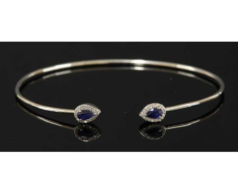 A white gold sapphire and diamond torque bangle, with a pear mixed cut sapphire, three claw set with a border of single cut d
