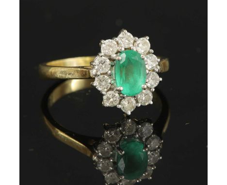 An 18ct gold emerald and diamond oval cluster ring, with an oval mixed cut emerald, four claw set to the centre, surrounded b