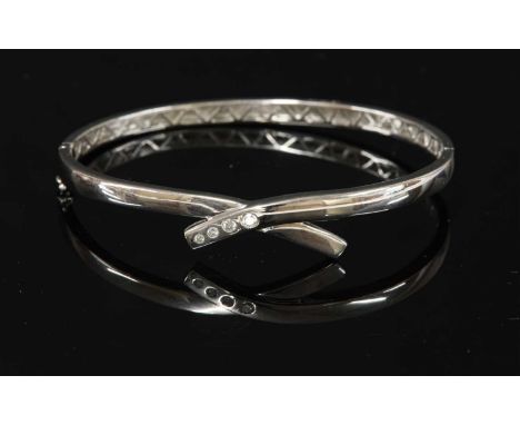 An 18ct white gold diamond set crossover bangle, with four graduated brilliant cut diamonds, Swiss set to one side, a pierced