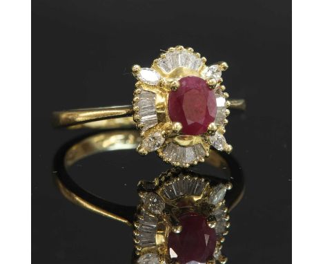 An 18ct gold ruby and diamond oval cluster ring, with an oval mixed cut ruby, four claw set to an open collet. A border of ta