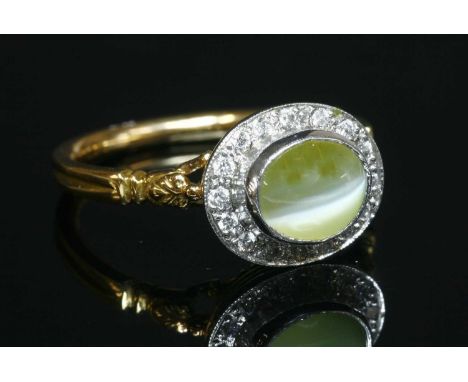 An 18ct yellow and white gold chrysoberyl cat's eye and diamond oval cluster ring, an oval cabochon chrysoberyl cat's eye, mi