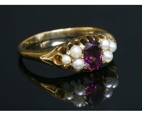 An Edwardian garnet and pearl boat-shaped ring, with an oval mixed cut garnet, claw set to the centre. A trefoil cluster of s