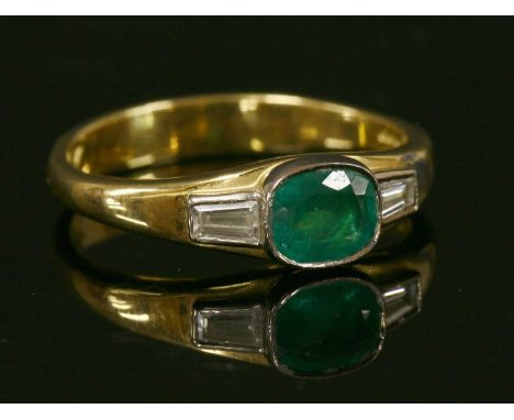 An 18ct gold emerald and diamond three stone ring, with an oval mixed cut emerald, rub set in a plain white collet. A tapered