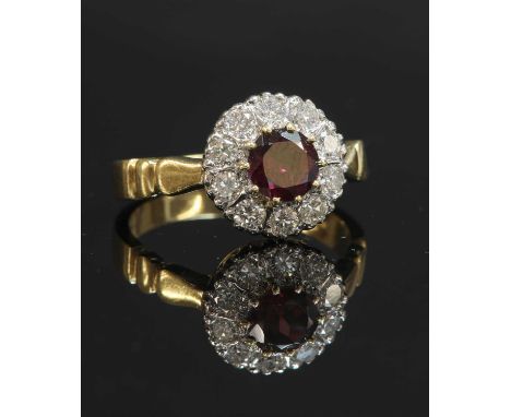 An 18ct gold garnet and diamond circular cluster ring, with a circular mixed cut garnet, claw set in yellow. A border of bril