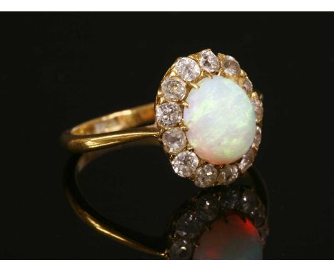 An opal and diamond cluster ring, with an oval cabochon opal, claw set to the centre. A border of old Swiss cut and old eight