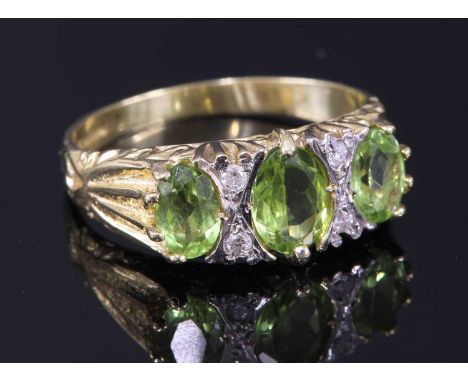 An 18ct gold three stone graduated peridot carved head style ring, three oval mixed cut peridots, claw set between pairs of r