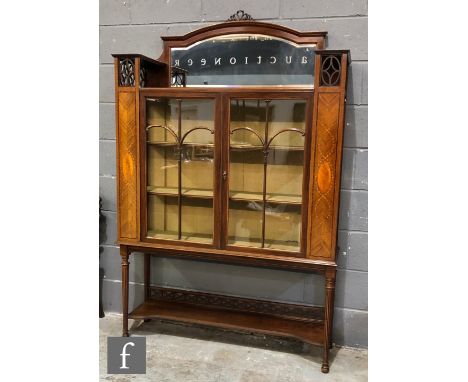 An early 20th Century mahogany display cabinet on later associated stand, with tied ribbon pediment over an arched mirror pan