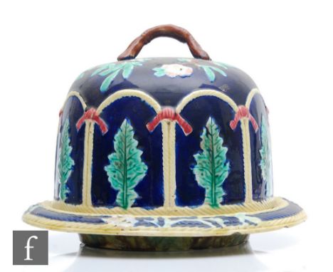 A late 19th Century Majolica cheese dish and cover decorated in relief with leaves and flowers over a blue ground, the base w